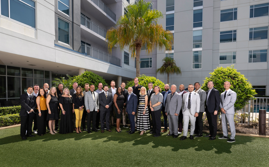 Group of professionals posing for a group photo outdoors in a courtyard with a modern building behind them.