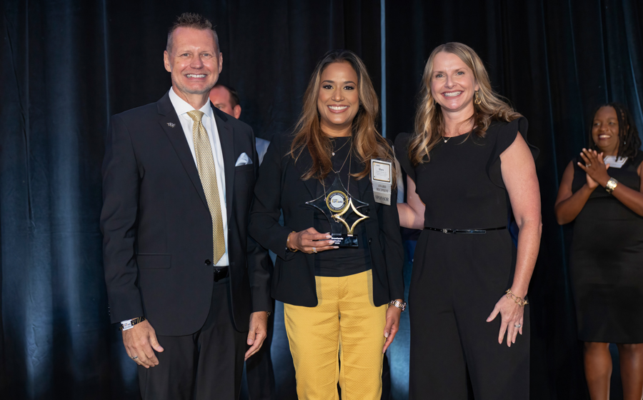 Three people on stage posing with a star-shaped award; center recipient holds the trophy while two colleagues smile beside her.
