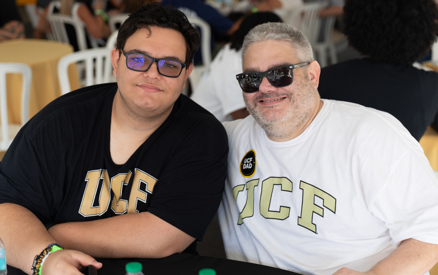 Two men pose for a photo at a casual event, wearing UCSF shirts and sunglasses, smiling at the camera.