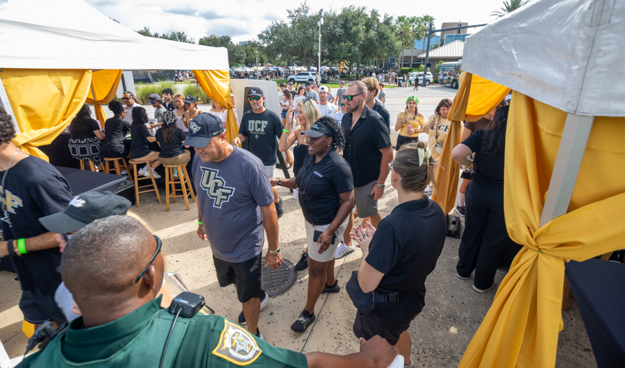 Outdoor UCF event with white tents and yellow drapes; attendees mingle near a row of stools under the canopies