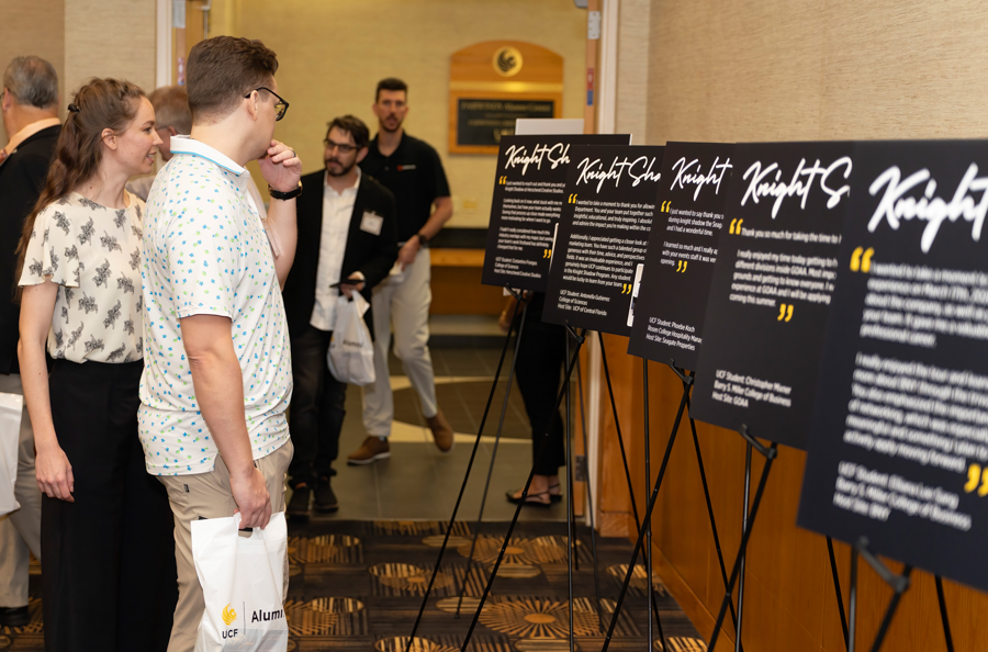 People at an indoor event read large black display boards on stands with yellow quotes in a hallway setting.