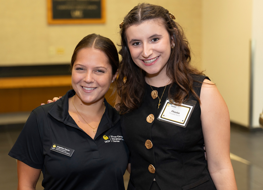 Two smiling women posing for a photo at an indoor event, both wearing name badges.