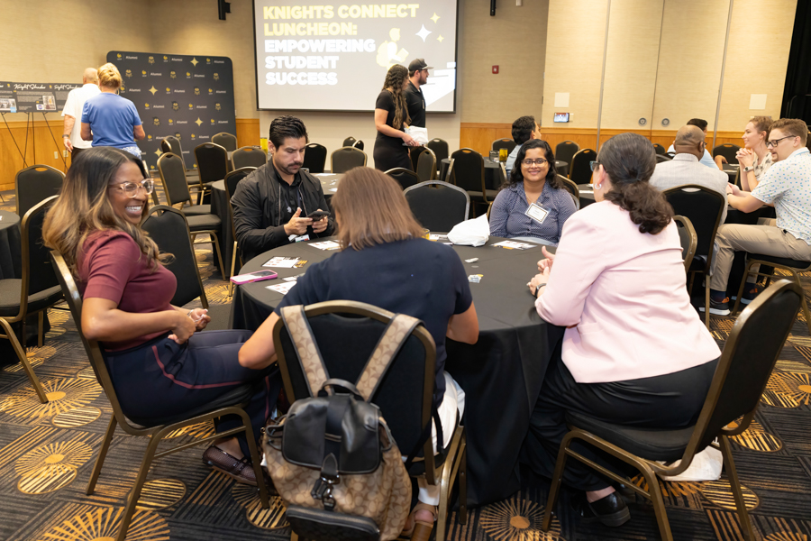 Group of professionals seated around a round table at a conference luncheon, with a presentation screen in the background reading 'Knights Connect Luncheon: Empowering Student Success'