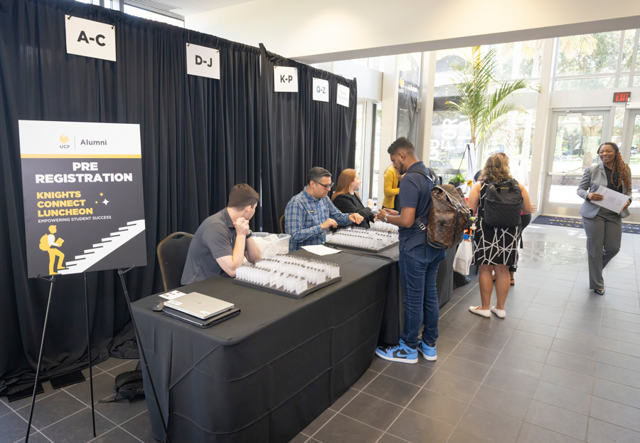 Registration desk at a university event; staff hand out name badges for Pre Registration: Knights Connect Luncheon under a black drape backdrop.