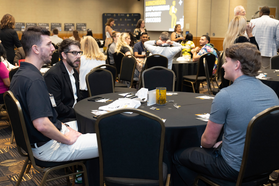 Professionals seated around a round table at a conference, chatting during a networking event in a ballroom.