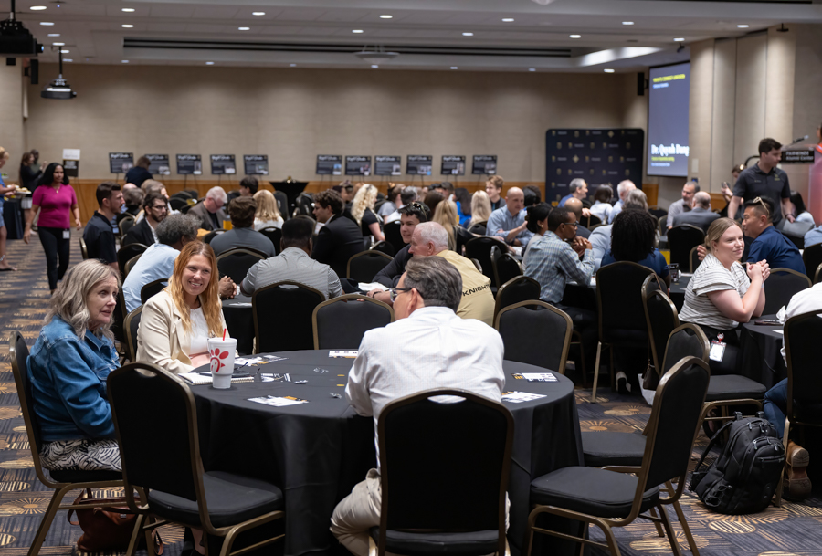 Large conference hall with round tables where groups of professionals chat and network between sessions.
