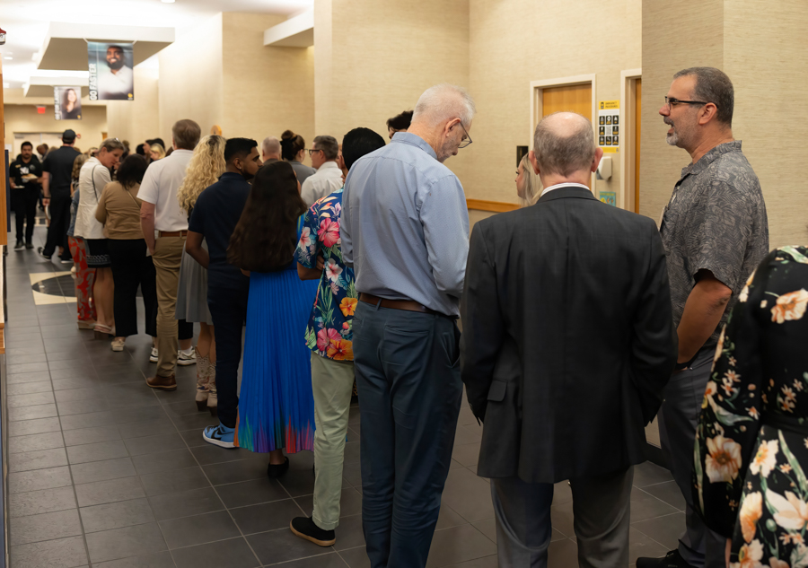 People form a long queue along a beige hallway at what looks like a conference or event check-in area.