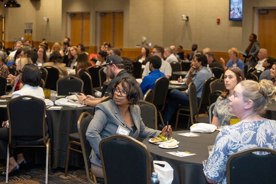 Diverse professionals seated at round tables at a conference banquet, eating and conversing in a large hall