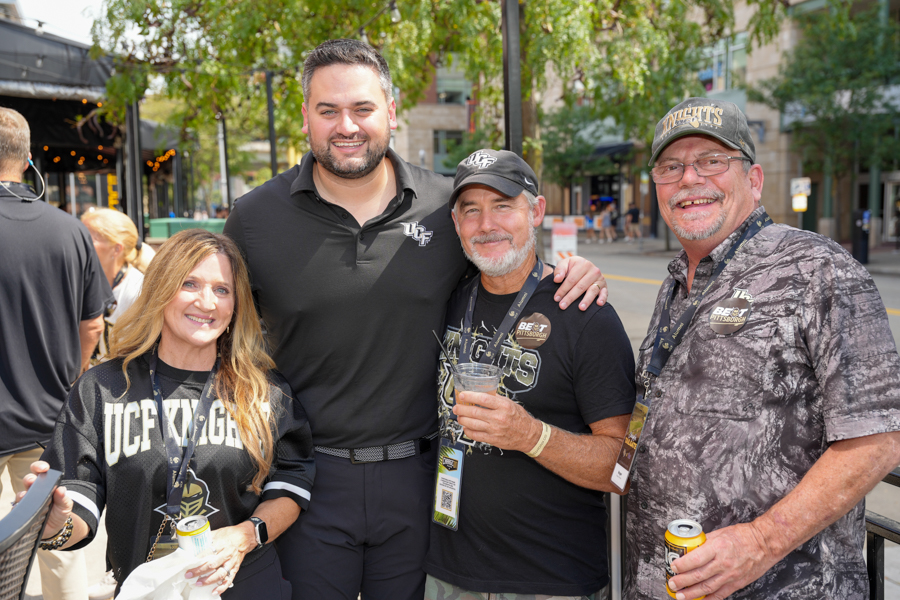 Group of four adults posing for a photo at an outdoor event, smiling with drinks in hand