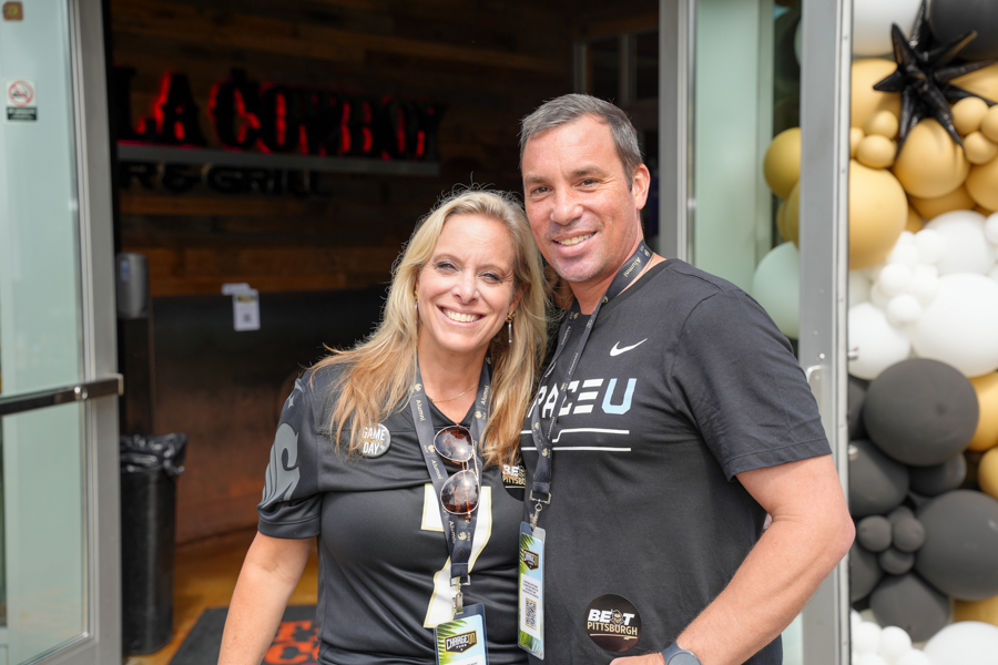 Two smiling adults with event lanyards posing in a doorway, balloons to the right.