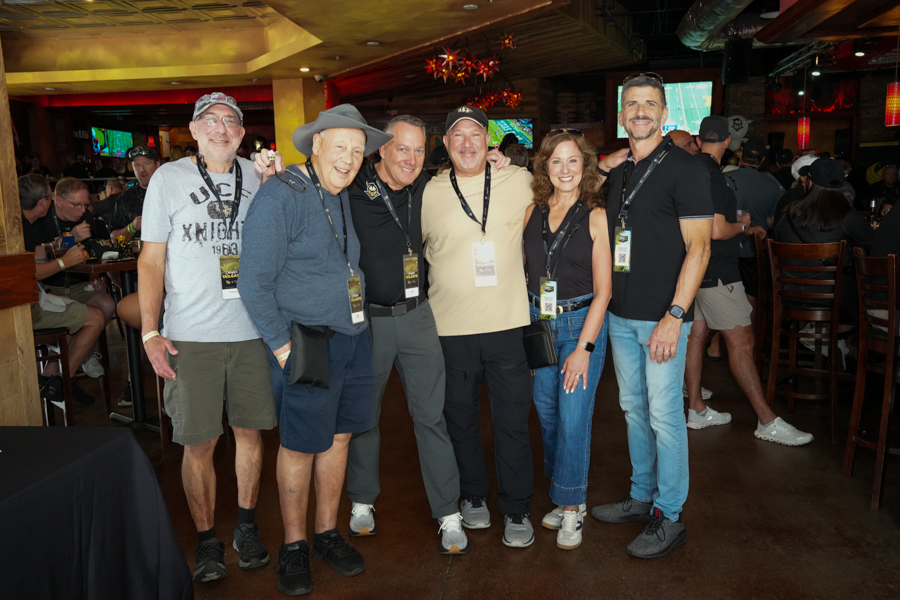 Seven adults posing together in a dim bar, wearing lanyards and casual clothing, smiling at the camera.