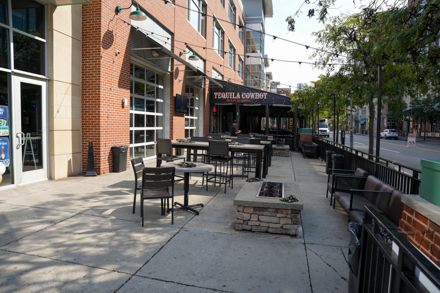 Outdoor patio of Tequila Cowboy Bar & Grill with black tables and chairs along a brick storefront on a sunny street edge.