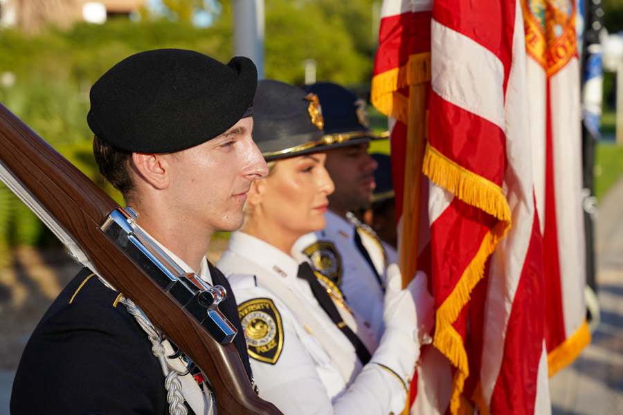 Color guard member in a beret holding a rifle at attention beside American flags during a ceremony