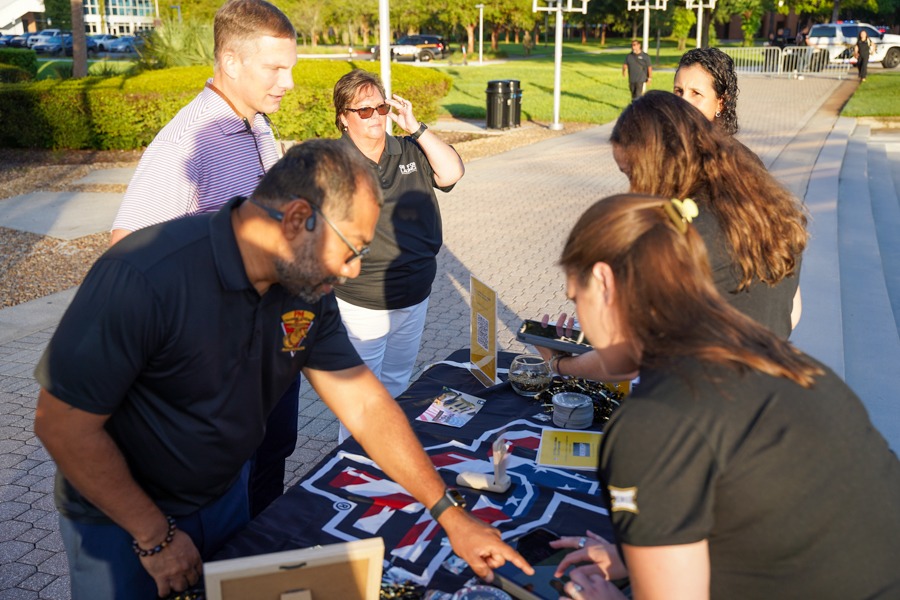 Group of adults at an outdoor information booth, volunteers handing out materials on a table.