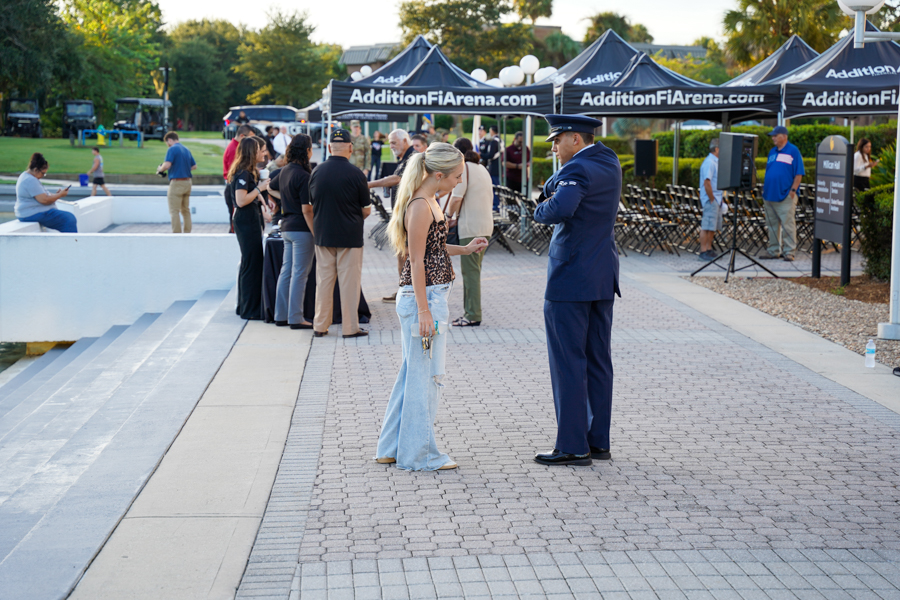 Woman in ripped jeans and a leopard top speaks with a uniformed officer at an outdoor event, with attendees and branded tents in the background.
