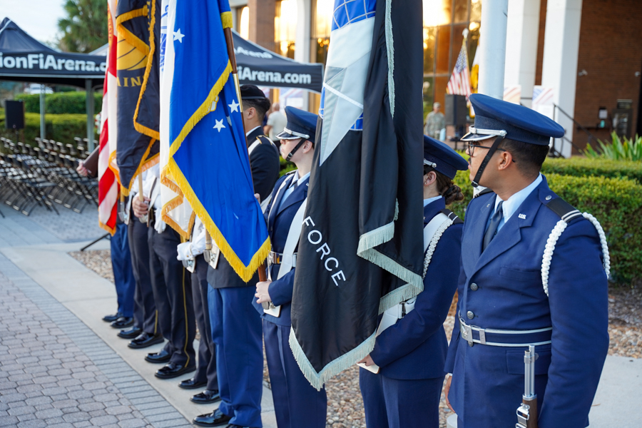 Uniformed honor guard holding multiple flags during an outdoor ceremony.