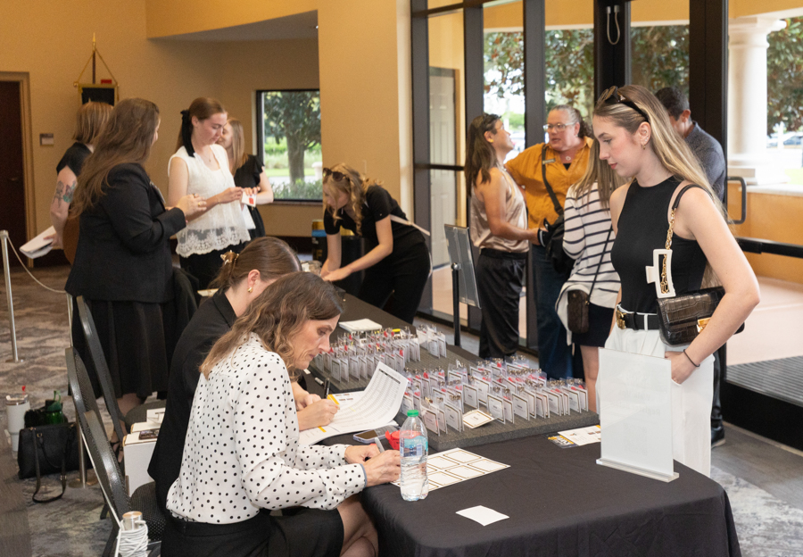 Registration desk at an indoor event with attendees and staff arranging name badges and forms on a table in front of large windows