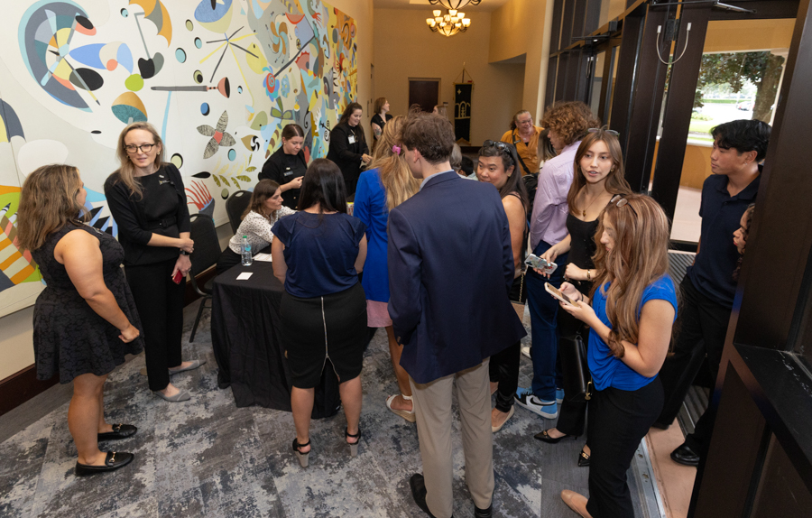 Group of young adults mingling at a reception near a registration table in a mural-filled hallway.