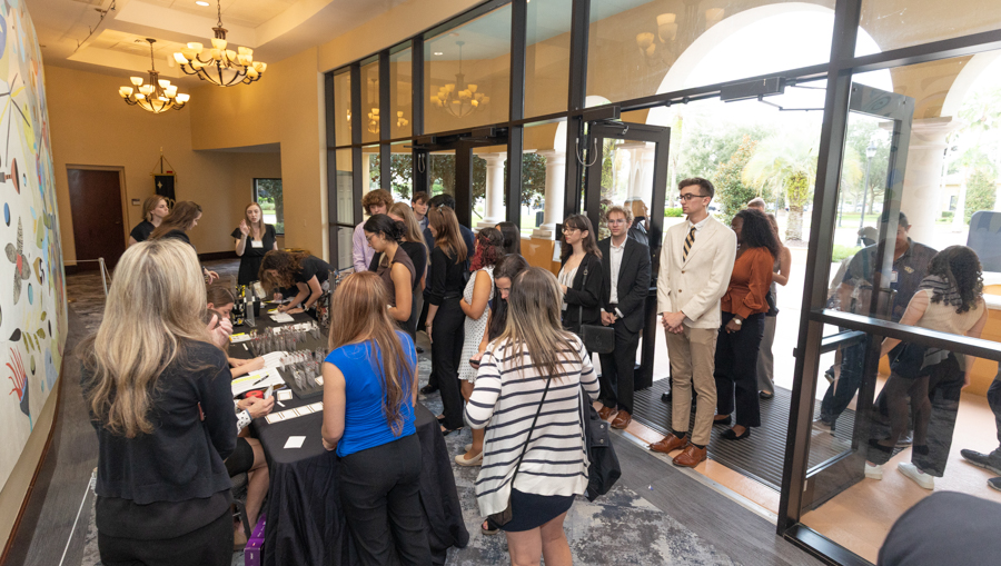 Attendees line up at a registration desk in a bright lobby, staff handing out name badges amid papers on the table.