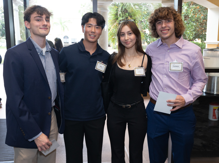 Four young adults posing together at a social event, wearing name badges and smiling.