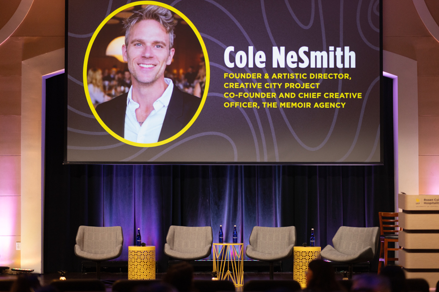Stage setup with a large screen showing a circular photo of Cole Nesmith and bold yellow bio text; four chairs on stage.