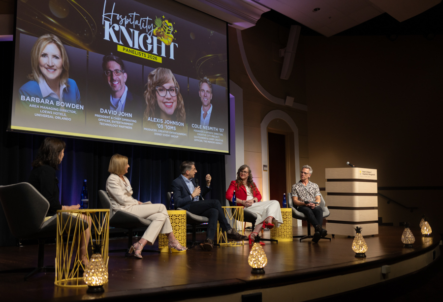 Panel discussion on a stage with five speakers seated in chairs; a large screen behind shows bios for the Hospitality Knight event.