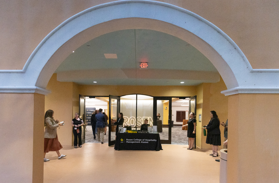 Arched entryway to a lobby with a registration table for Rosen College of Hospitality Management Alumni and guests gathered nearby.