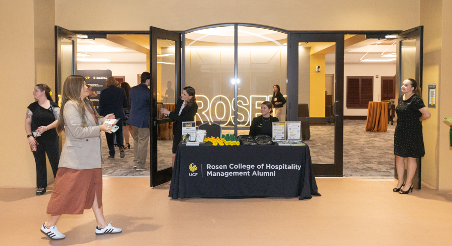 Registration desk for Rosen College of Hospitality Management Alumni in a campus lobby, with attendees arriving and staff organizing.