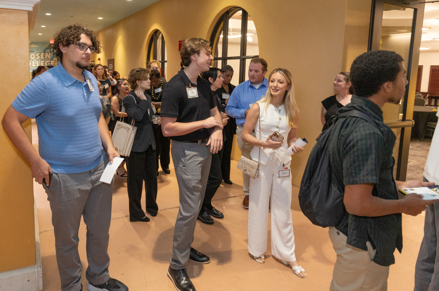 Group of diverse people in a hallway at a conference, waiting in line with name badges visible to the camera.