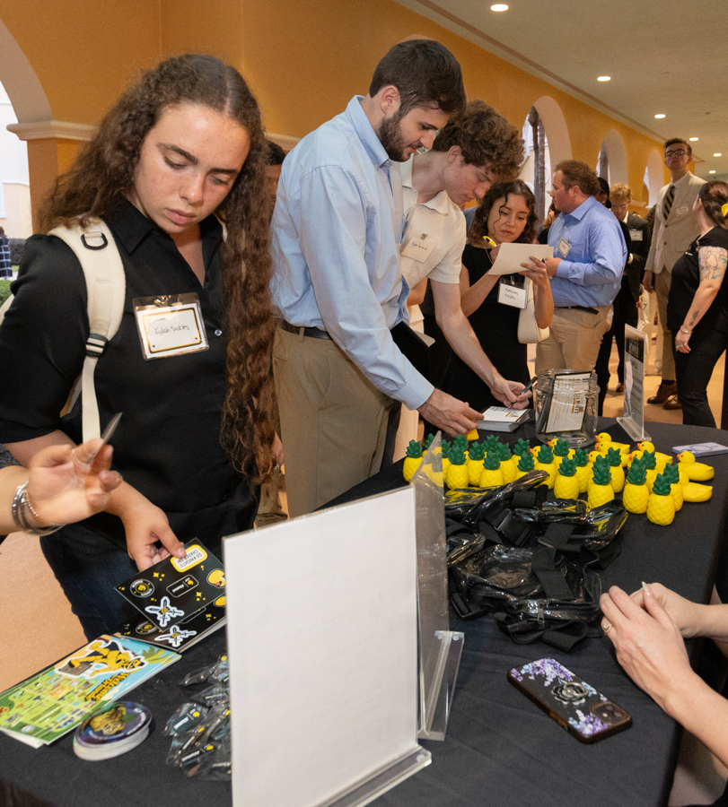 People at a conference booth distributing promo items; yellow pineapple stress balls on the table nearby.