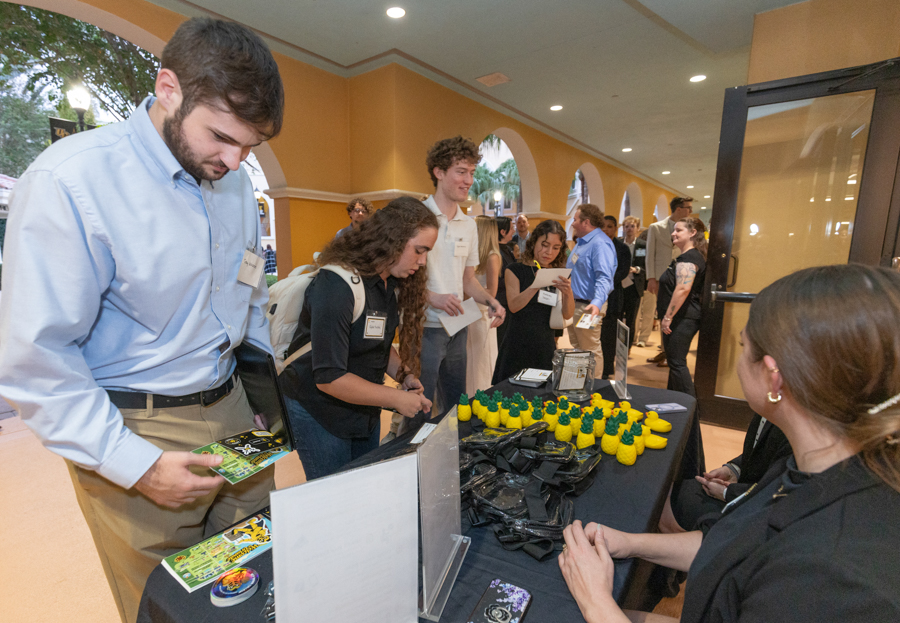 People line up at a registration table in a bright hall; staff hand out name badges and event materials.