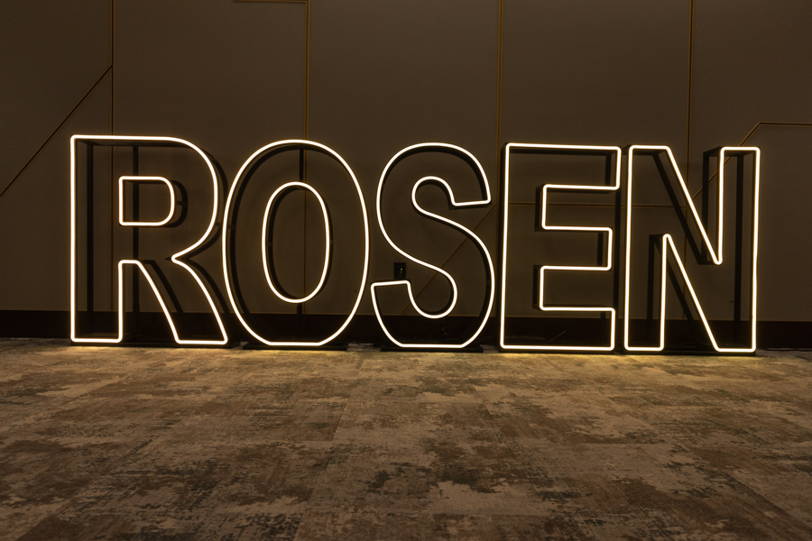 Large illuminated neon sign spelling ROSEN, installed in a dim indoor space as an art piece on the wall and floor.