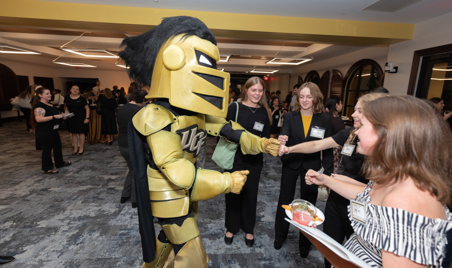 Gold knight mascot shakes hands with smiling attendees at a conference reception.