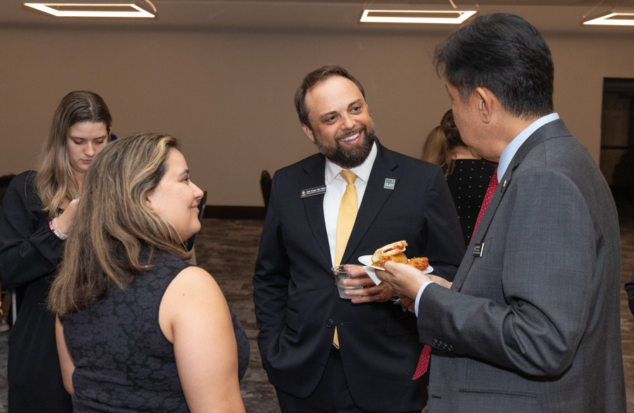 Group of professionals at a networking event, foreground trio chatting over drinks and appetizers in a modern venue.
