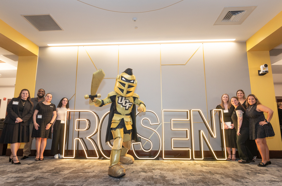 Group photo with a gold-armored knight mascot posing beside a glowing ROSEN sign, flanked by smiling attendees.