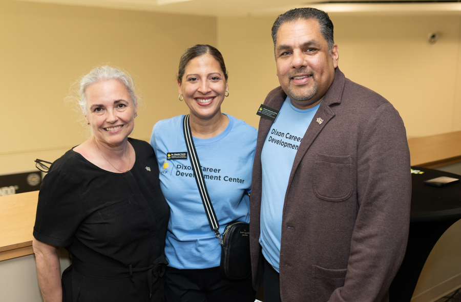 Three people smiling for a group photo at an indoor event; two wear light blue Dixon Career Development Center shirts.