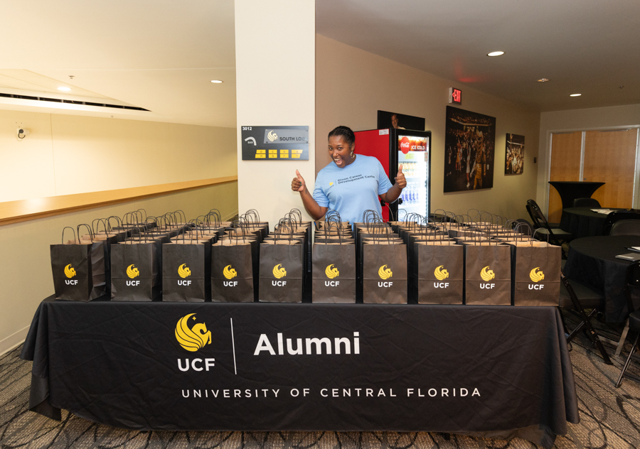 Volunteer behind a table with UCF Alumni bags ready for distribution at a University of Central Florida event.