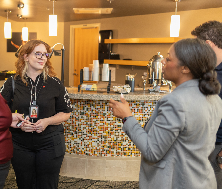 Staff member with ID badge chats with customers at a mosaic-tiled cafe bar counter.