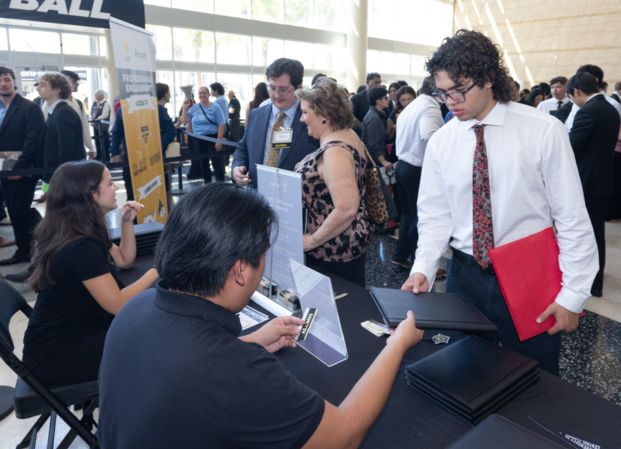 Registration desk at a career fair: attendees speak with recruiters seated behind the table with folders and brochures.