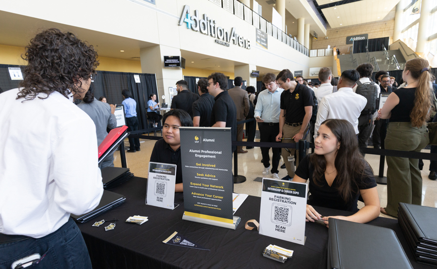 Campus career fair registration desk with staff handing out materials and attendees in a large atrium.