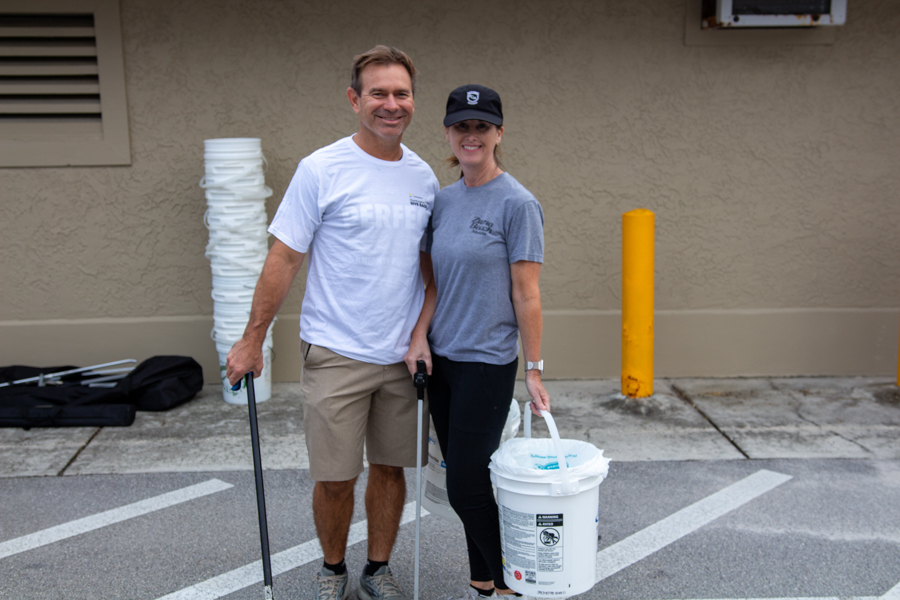 Two people smiling in a parking lot, each holding painting tools with buckets nearby, ready to paint a building exterior