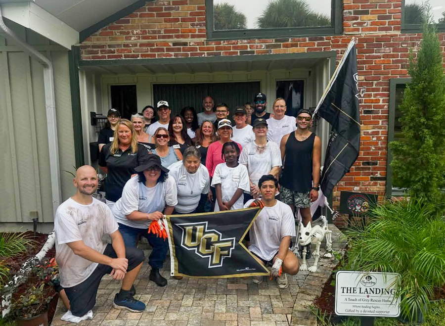 Group of volunteers posing on a front porch with a UCF flag after a community cleanup or rescue event.