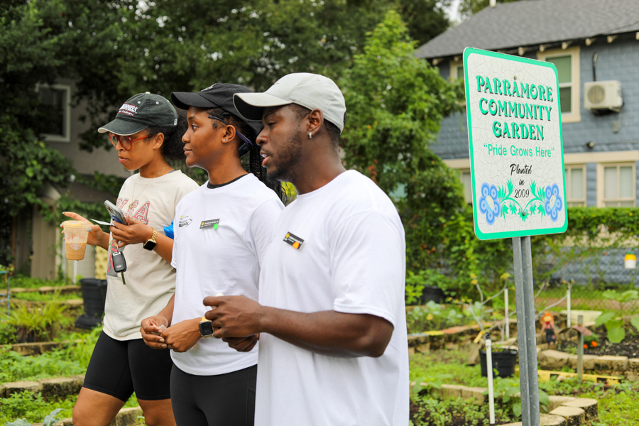 Three volunteers walk through a Parramore Community Garden, beside a sign reading 'Pride Grows Here'.