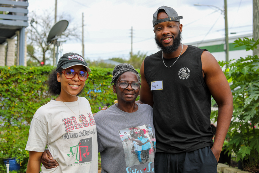 Three smiling volunteers stand outside together, two women and a man, wearing casual clothes and name tags.