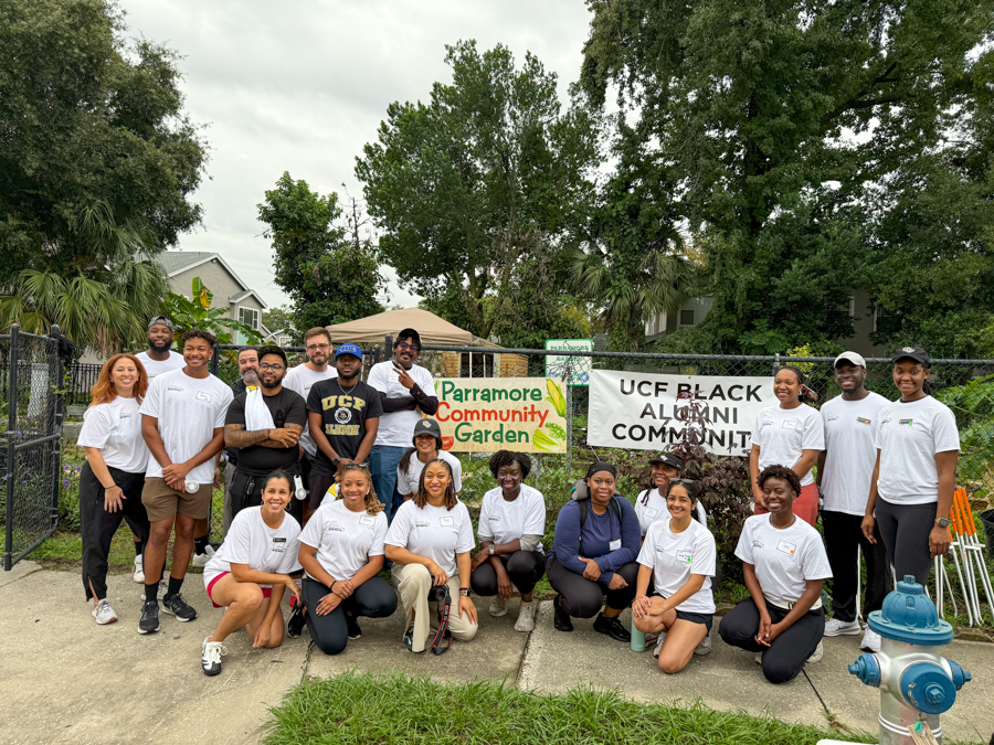 Diverse group of volunteers in white shirts posing in front of banners for Parramore Community Garden and the UCF Black Alumni Community.