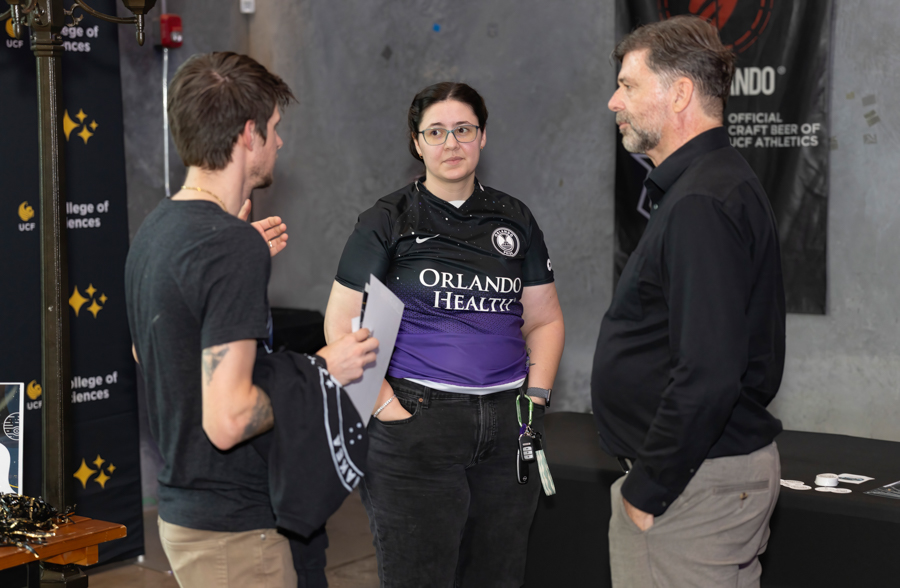 Three people in conversation at an Orlando Health event, with banners in the background.