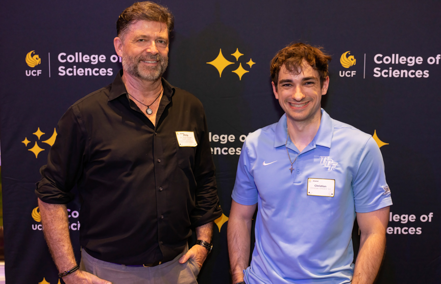 Two men posing for a photo in front of a College of Sciences backdrop at a formal event.